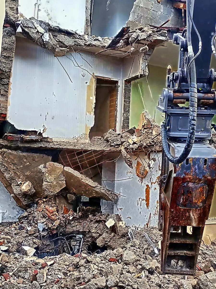Draufsicht auf eine Baulücke zwischen zwei Reihenhauszeilen in Köln, darin ein oranger Bagger im Abbruchschutt
