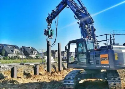 Bagger der PILOT GmbH rüttelt mit Anbauvibrator einen Stahlträger für den Berliner Verbau ein, weitere Träger stehen bereits im Boden