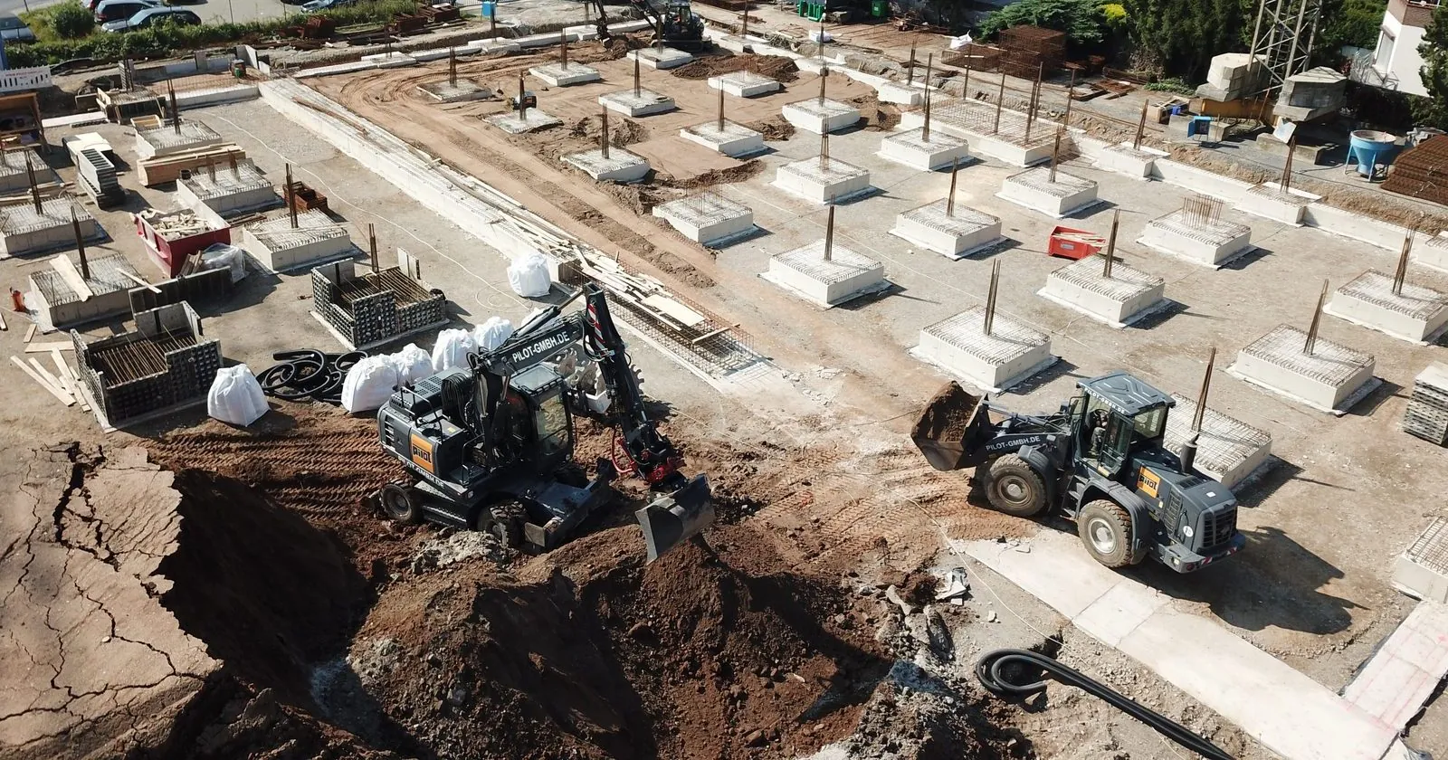 Punktfundamente auf der Baustelle in Köln-Merheim, durch die später die Abwasserrohre mit Mauerkragen geführt werden, mit Bagger und Radlader der PILOT GmbH