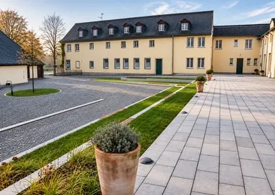 Innenhof am Kloster Heisterbach mit gepflasterten Flächen, Rasenstreifen und einem Pflanzkübel vor einem langen Gebäude