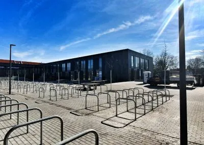 Fertige Pflasterfläche am Schulgebäude mit zahlreichen Fahrradanlehnbügeln, Leuchtenmasten und jungen Bäumen