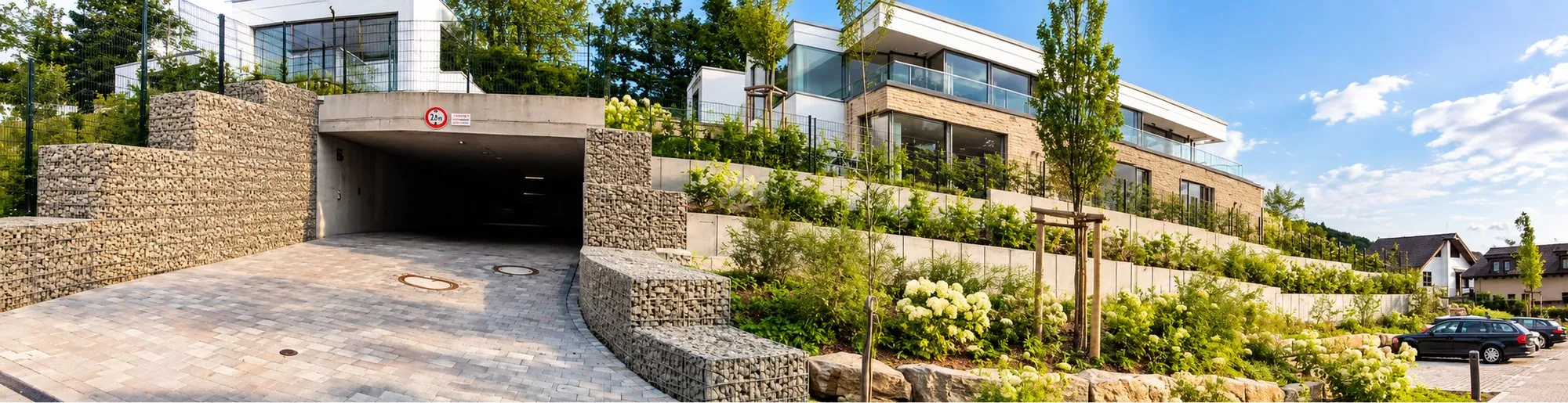 Die Tiefgaragenzufahrt im Parkensemble Schaaffhausen zwischen zwei Gabionenwänden, darüber die begrünten Terrassen der neuen Wohnhäuser