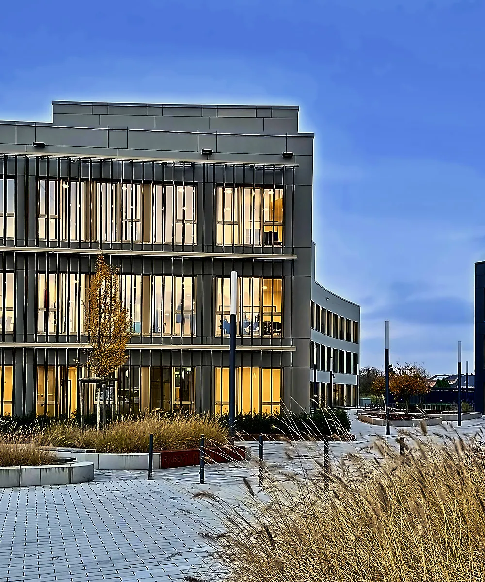 Vorplatz eines Bürogebäudes in Köln-Wahn mit hellem Betonpflaster, Sitzblöcken, Gräserpflanzung und Pollern