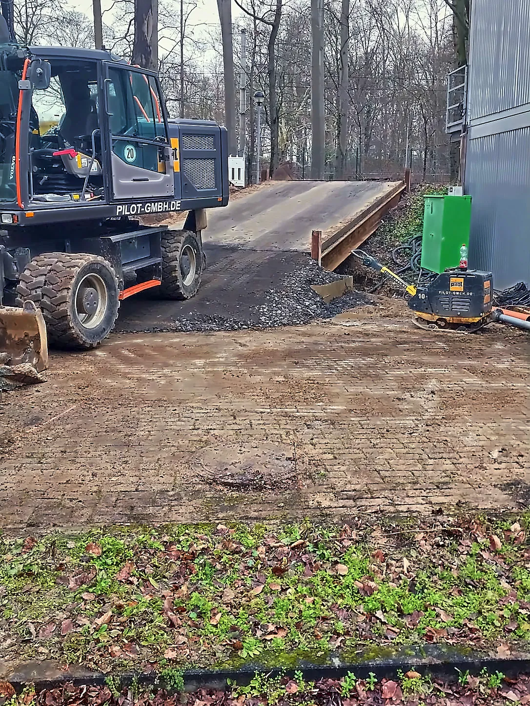 Mobilbagger auf der Baustraße vor einer Behelfsbrücke aus Stahl im Sportpark Köln-Müngersdorf, im Hintergrund Bäume