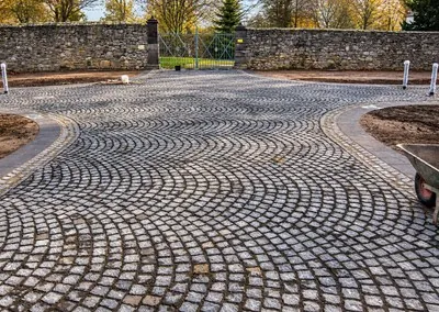 Große, in Segmentbögen gepflasterte Fläche vor einem geschlossenen Eisentor in einer Bruchsteinmauer