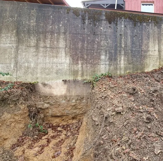 Betonstützmauer des Nachbargrundstücks mit freigelegtem Fundament am Rand der späteren Baugrube in Remscheid